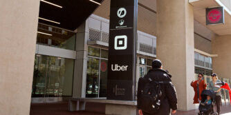 A person walks by a tall city building with the logos of Square and Uber on the front.