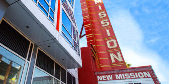 Picture of the New Mission Theater marquee with a modern, colorful building behind it