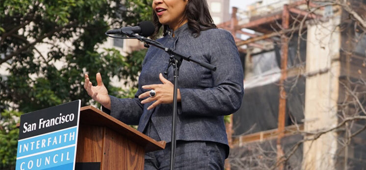 San Francisco mayoral candidate London Breed stands at a podium with a sign on the front that says "San Francisco Interfaith Council"